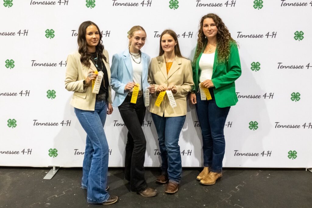 Senior 4-H livestock judging team standing with award ribbons.