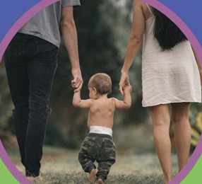 parents holding hands with toddler walking together.